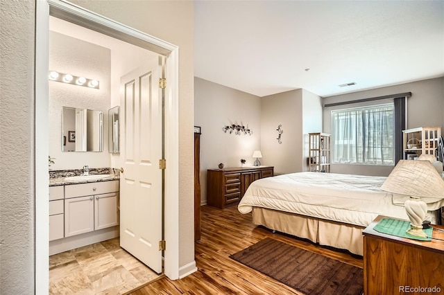 bedroom featuring baseboards, visible vents, a sink, light wood-style floors, and ensuite bathroom