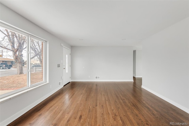 empty room with dark wood-style floors, visible vents, and baseboards