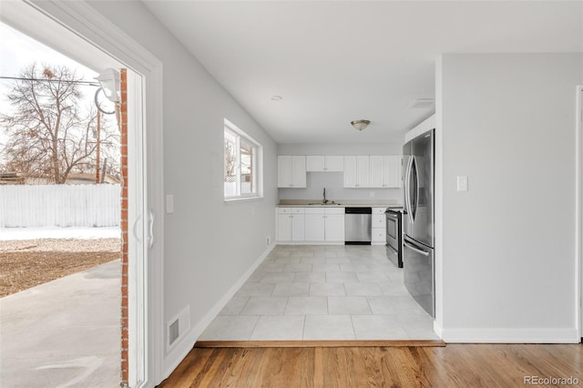 kitchen featuring stainless steel appliances, light countertops, white cabinets, a sink, and baseboards