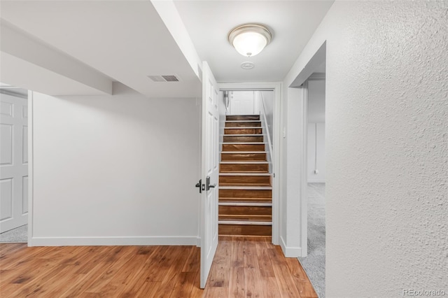 stairs with a textured wall, wood finished floors, visible vents, and baseboards