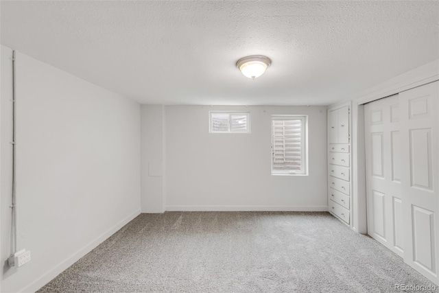 unfurnished bedroom with a closet, light colored carpet, a textured ceiling, and baseboards