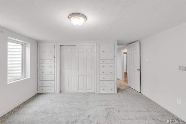 unfurnished bedroom with a closet, baseboards, a textured ceiling, and light colored carpet