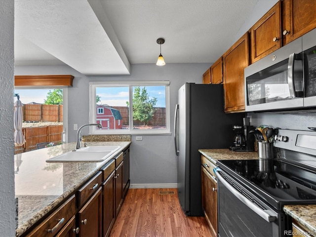 11877 W Bowles Cir, Littleton, CO 80127 - kitchen with stainless steel appliances, wood finished floors, light stone counters, brown cabinetry, and pendant lighting