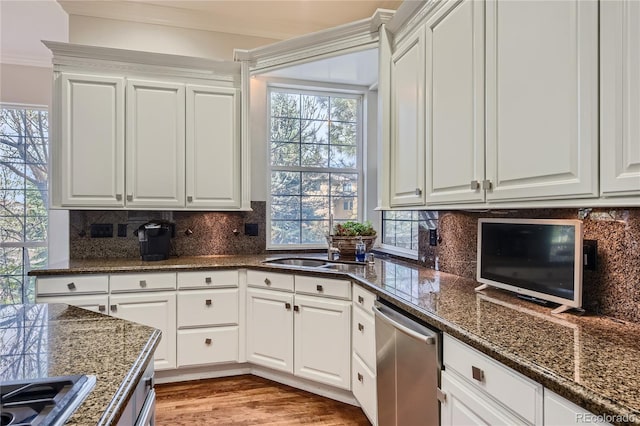 kitchen with light wood-type flooring, tasteful backsplash, white cabinets, dishwasher, and sink