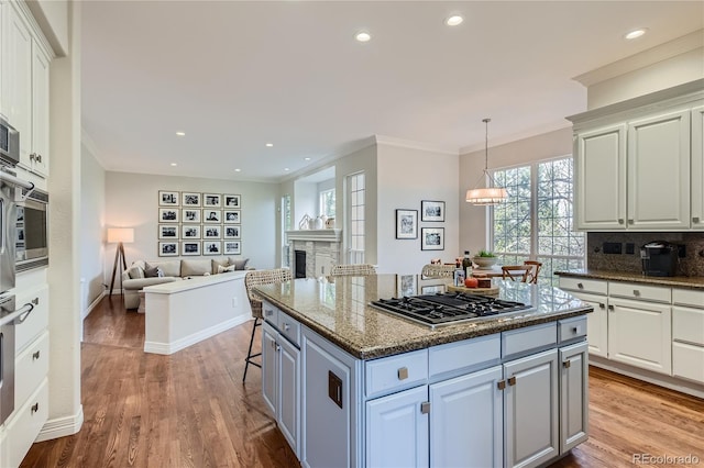 kitchen with a breakfast bar, dark stone counters, light wood-type flooring, tasteful backsplash, and stainless steel gas stovetop