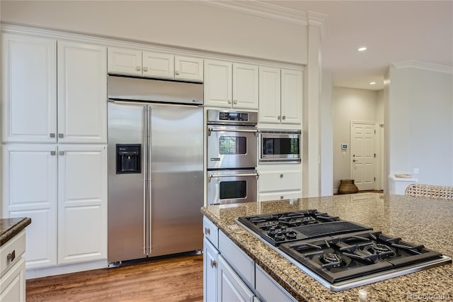 kitchen with light stone countertops, light hardwood / wood-style floors, built in appliances, crown molding, and white cabinets