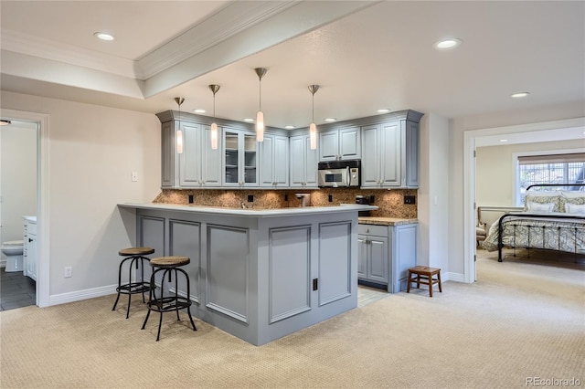 kitchen featuring a kitchen bar, tasteful backsplash, kitchen peninsula, light carpet, and hanging light fixtures