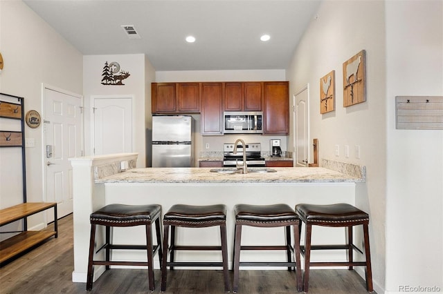 kitchen with kitchen peninsula, dark wood-type flooring, a breakfast bar, appliances with stainless steel finishes, and sink