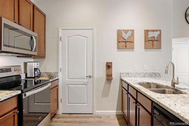 kitchen with sink, light wood-type flooring, light stone counters, and appliances with stainless steel finishes