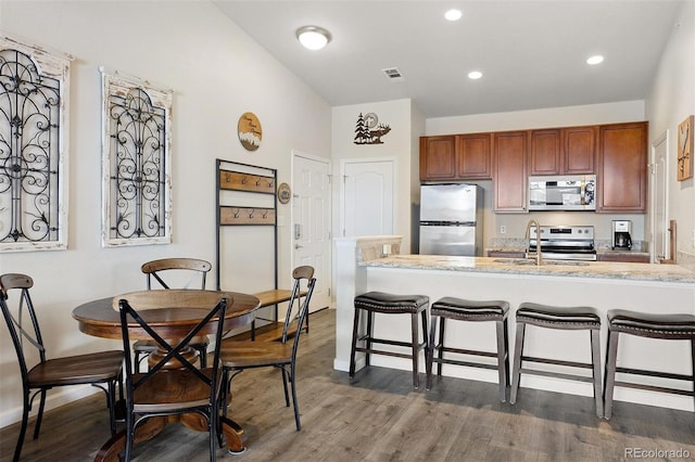 kitchen with stainless steel appliances, sink, a kitchen bar, kitchen peninsula, and dark hardwood / wood-style floors