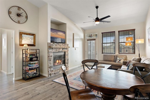 dining room with lofted ceiling, ceiling fan, light hardwood / wood-style flooring, and a stone fireplace