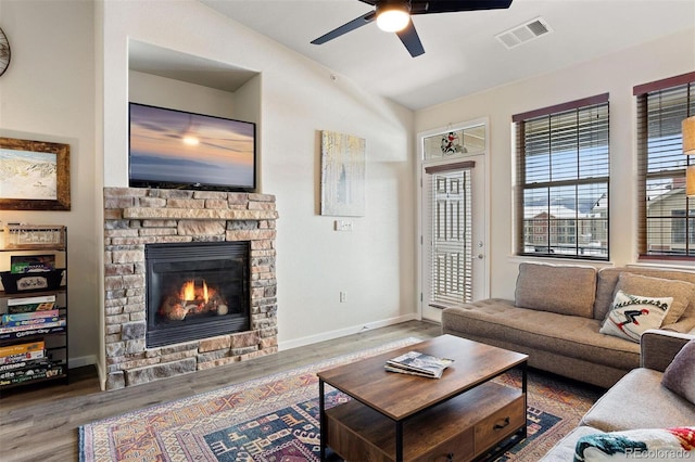 living room featuring hardwood / wood-style floors, ceiling fan, and a stone fireplace