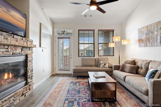 living room featuring vaulted ceiling, ceiling fan, dark hardwood / wood-style floors, and a stone fireplace