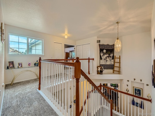 corridor with a notable chandelier, a textured ceiling, and carpet