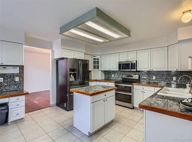 kitchen featuring sink, a center island, light tile patterned floors, appliances with stainless steel finishes, and white cabinets