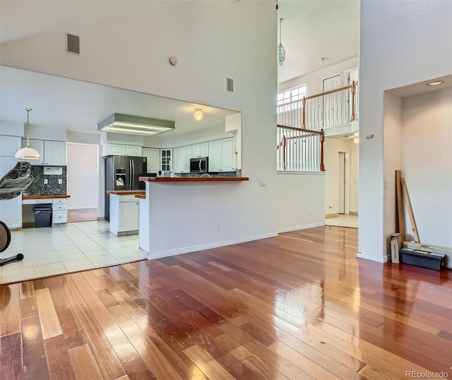 living room featuring white cabinetry, a towering ceiling, light hardwood / wood-style flooring, and kitchen peninsula