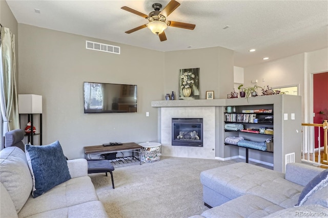 living room featuring a tiled fireplace, ceiling fan, carpet flooring, and a textured ceiling