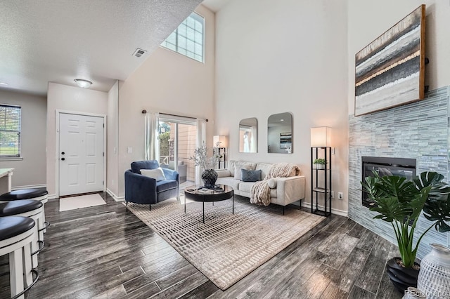 3611 S Perth Cir Unit 103, Aurora, CO 80013 - living area featuring a towering ceiling, dark wood-style flooring, plenty of natural light, a tile fireplace, and a textured ceiling