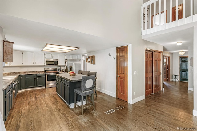 kitchen with a center island, sink, dark wood-type flooring, stainless steel appliances, and a towering ceiling