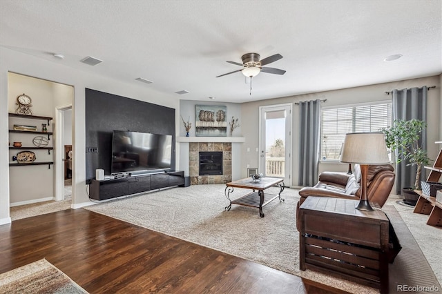 living area with a tiled fireplace, visible vents, ceiling fan, and wood finished floors