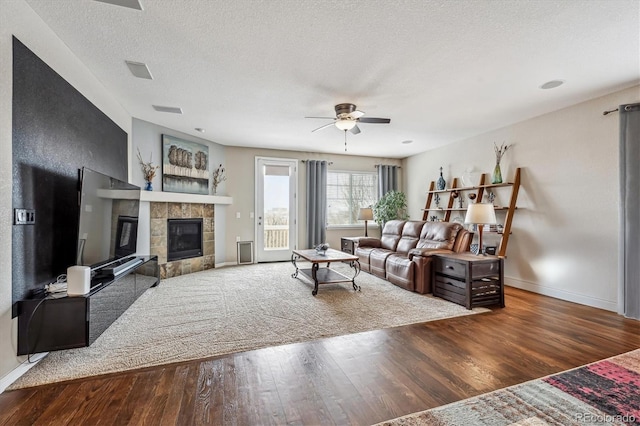 living area with ceiling fan, baseboards, a tiled fireplace, a textured ceiling, and wood finished floors