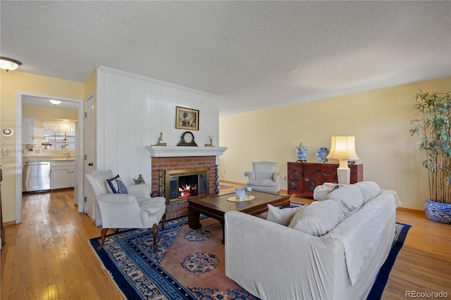 2608 E Fremont Pl, Centennial, CO 80122 - living room featuring light wood finished floors, a brick fireplace, a textured ceiling, and baseboards