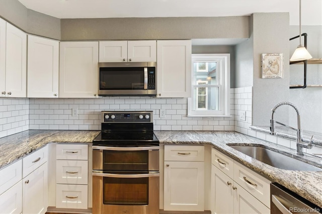 kitchen with light stone countertops, appliances with stainless steel finishes, tasteful backsplash, sink, and white cabinetry