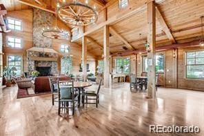 dining room with wood ceiling with exposed beams, wooden walls, a fireplace, high vaulted ceiling, and wood finished floors