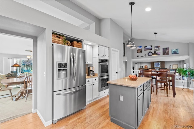 kitchen featuring white cabinetry, decorative light fixtures, lofted ceiling, stainless steel appliances, and light wood finished floors