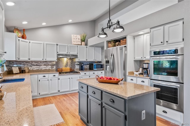 kitchen with gray cabinets, under cabinet range hood, decorative backsplash, stainless steel appliances, and a sink