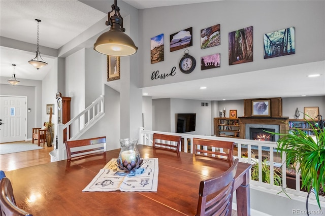 dining space featuring a towering ceiling, recessed lighting, a fireplace, stairway, and wood finished floors