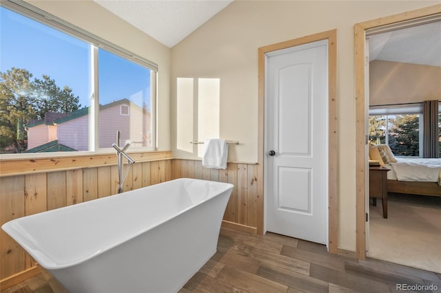 bathroom featuring a soaking tub, connected bathroom, vaulted ceiling, wood finished floors, and wainscoting