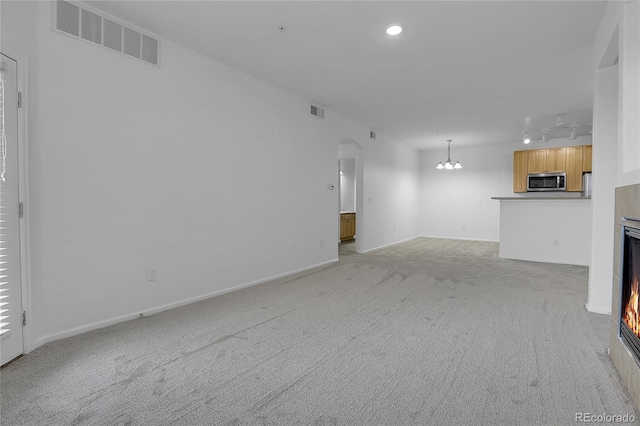 unfurnished living room featuring an inviting chandelier and light carpet