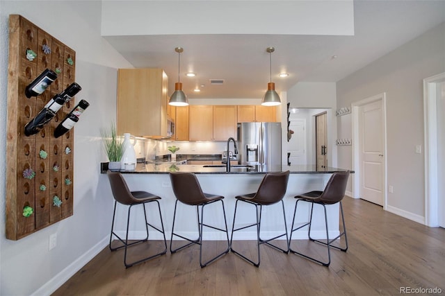 kitchen with appliances with stainless steel finishes, pendant lighting, light brown cabinetry, sink, and kitchen peninsula