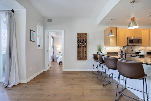 kitchen featuring pendant lighting, sink, a breakfast bar, light brown cabinetry, and light wood-type flooring