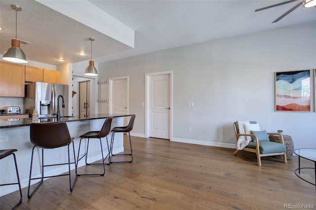 kitchen with a kitchen bar, stainless steel fridge with ice dispenser, hanging light fixtures, light brown cabinets, and dark hardwood / wood-style floors