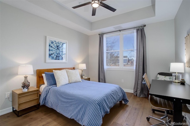 bedroom with hardwood / wood-style flooring, a raised ceiling, and ceiling fan