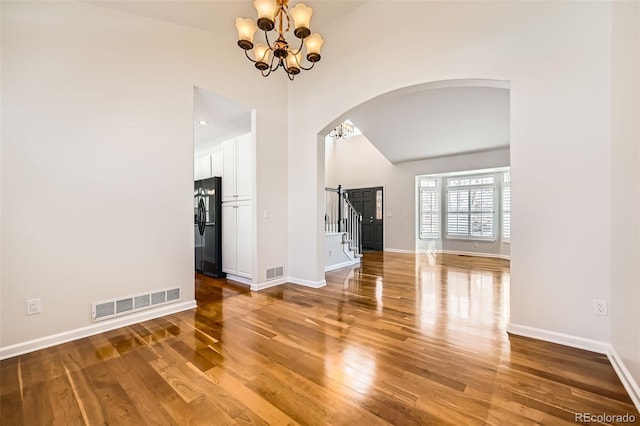 unfurnished living room with a notable chandelier, visible vents, arched walkways, and wood finished floors