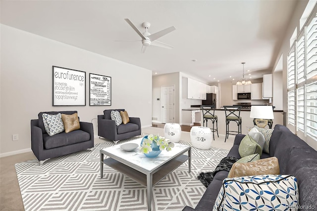 carpeted living room featuring baseboards and ceiling fan with notable chandelier