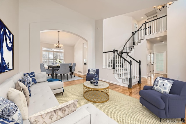 living area with a chandelier, arched walkways, wood finished floors, baseboards, and stairway