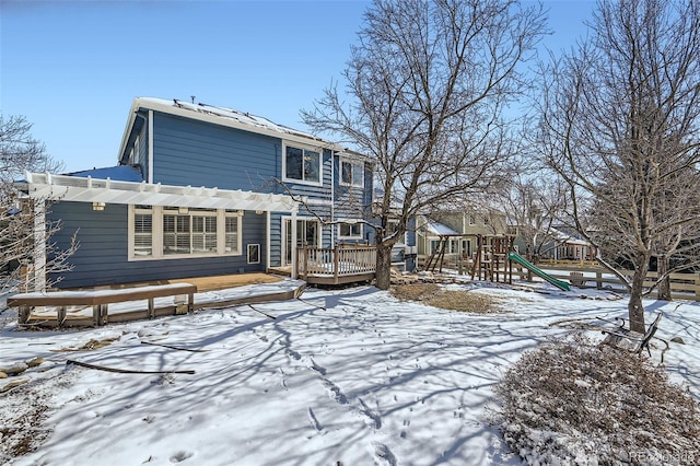 snow covered house with a playground, a wooden deck, and a pergola