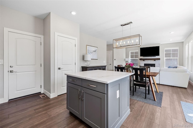 1632 Saddlesmith Pl, Castle Pines, CO 80108 - kitchen featuring gray cabinetry, dark wood-style floors, a center island, pendant lighting, and a fireplace