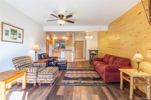 living area with wooden walls, wood finished floors, and ceiling fan with notable chandelier