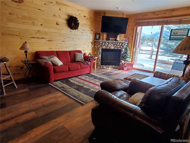 living area with wooden walls, a stone fireplace, and wood finished floors