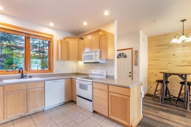 kitchen with an inviting chandelier, light brown cabinetry, a sink, wood walls, and white appliances