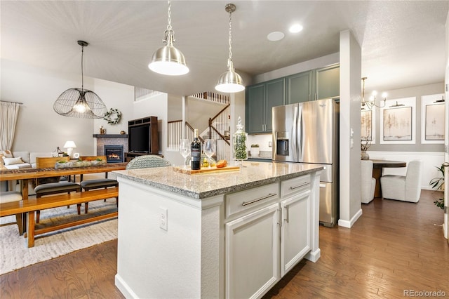 kitchen with light stone counters, decorative light fixtures, stainless steel fridge with ice dispenser, dark hardwood / wood-style floors, and a kitchen island