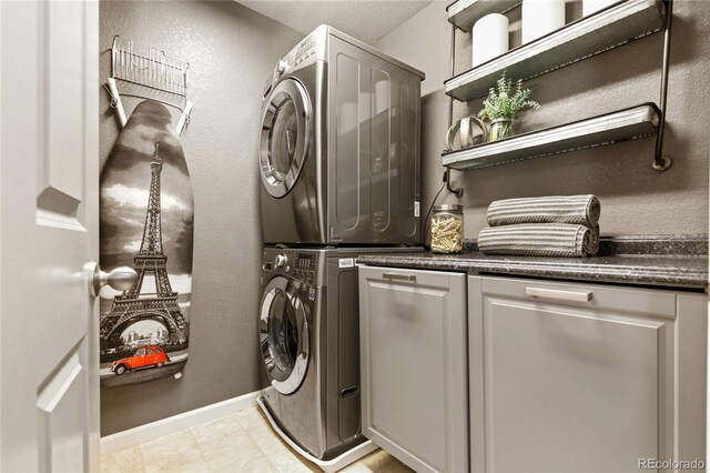 clothes washing area with stacked washer / drying machine and cabinets