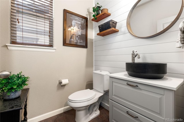 half bathroom with toilet, wood finished floors, vanity, and baseboards