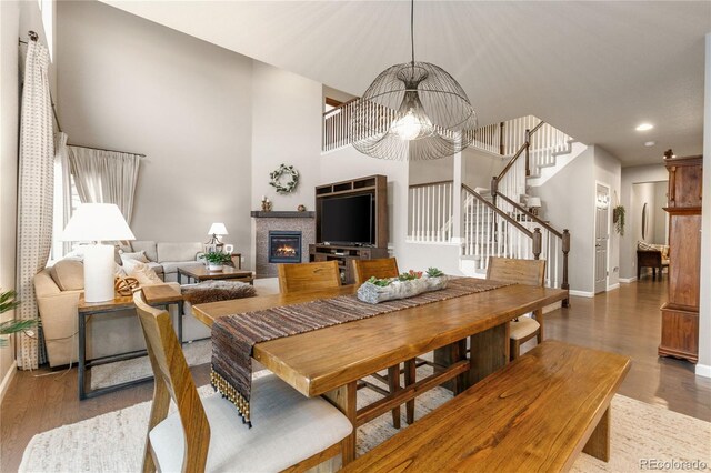 dining space with a fireplace, wood finished floors, baseboards, stairway, and an inviting chandelier