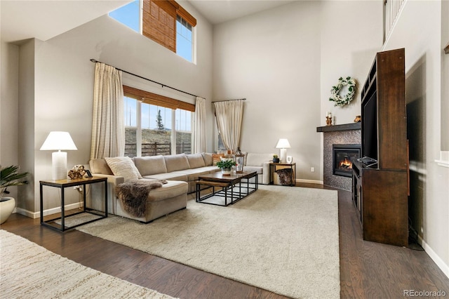 living area with dark wood-style floors, a high ceiling, a fireplace, and baseboards